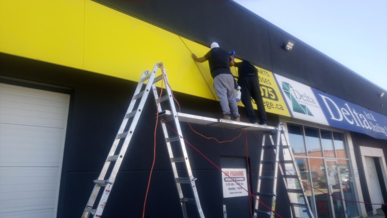 Crew installing a yellow fascia sign from ladders